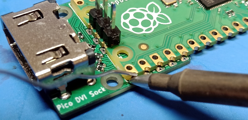 A soldering iron is pressed onto the edge of the Pico board, so that it touches the side of the castellation, and the top of the Sock board surface mount contact.